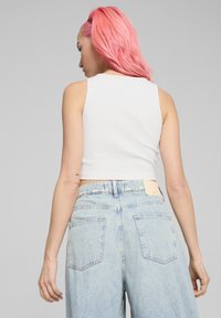 Witte geribbelde crop top gecombineerd met lichtblauwe high-waisted jeans, voorzien van een leren label op de achterkant en standaard achterzakken.