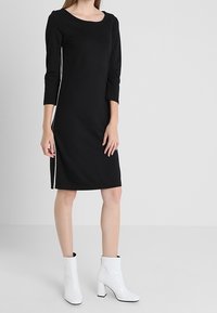 Svart knälång klänning med trekvartslånga ärmar, med vita sidsömmar. Buren med glansiga vita ankelstövlar och rund halsringning.