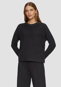 Zwarte sweatshirt met een ronde hals, verlaagde schouders en een ontspannen pasvorm. Zachte textuur met geribde halslijn en manchetten. Gepaard met bijpassende broek.