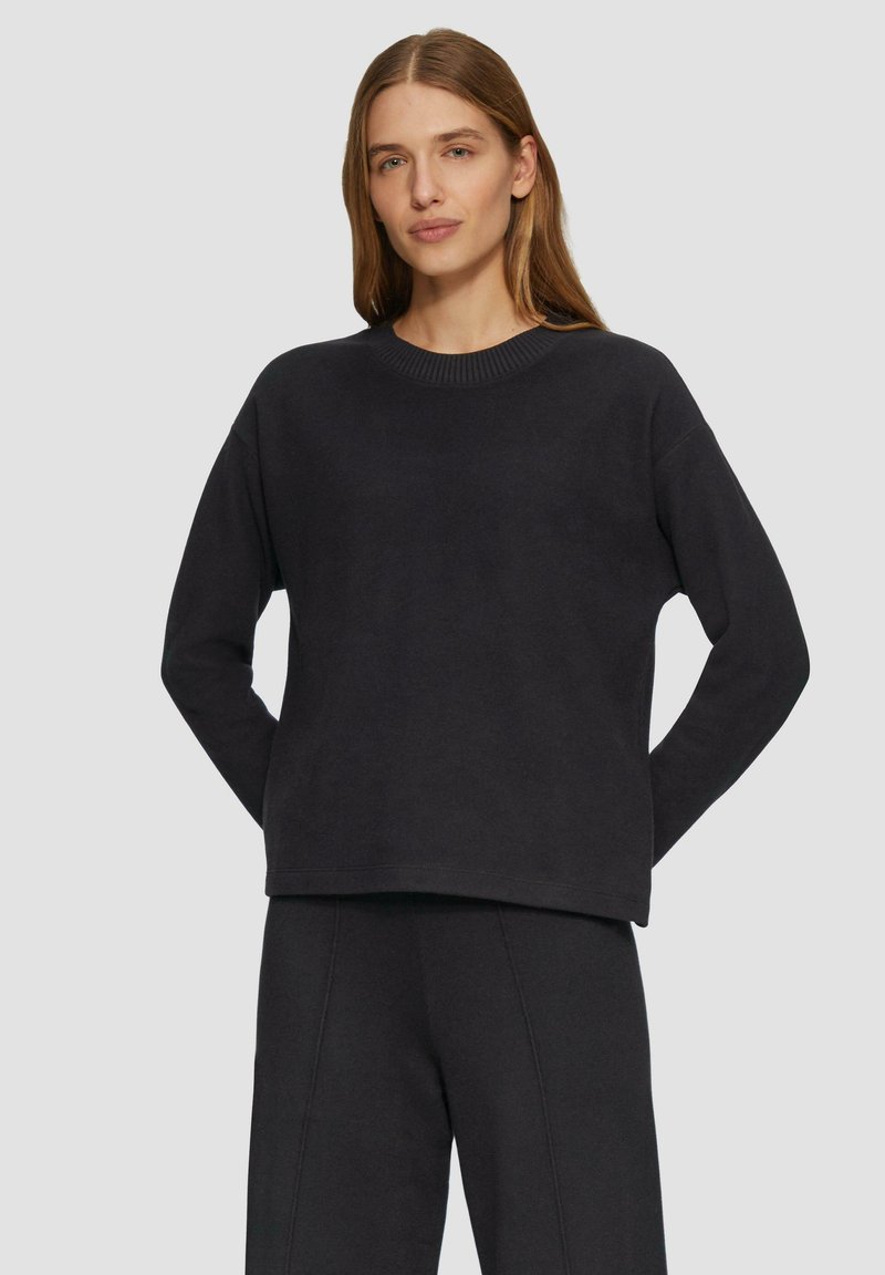 Zwarte sweatshirt met een ronde hals, verlaagde schouders en een ontspannen pasvorm. Zachte textuur met geribde halslijn en manchetten. Gepaard met bijpassende broek.