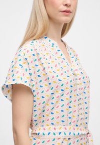 Blusa a maniche corte con scollatura a V, realizzata in tessuto leggero, con un motivo a goccia multicolore su sfondo chiaro.