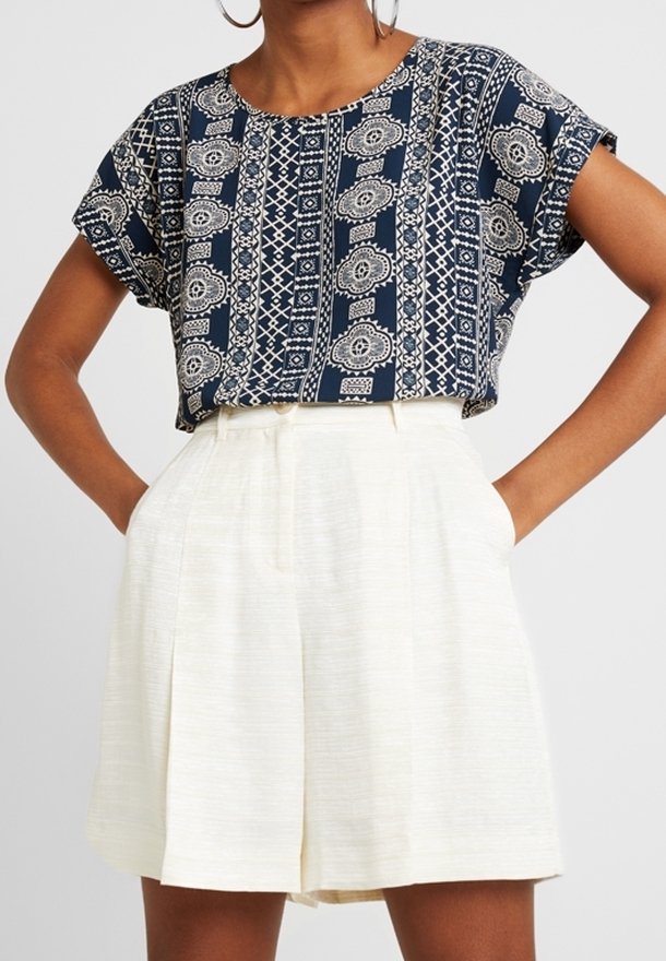 Mřížkovaná blůza navy modré barvy s krátkým rukávem, se bílými geometrickými vzory. Spárovaná s krémovými plnými šortkami s vysokým pasem.