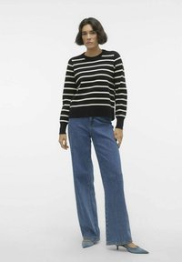 Pull rayé noir et crème à manches longues, associé à un jean en denim bleu à taille haute et jambes larges, et des escarpins pointus bleu clair.