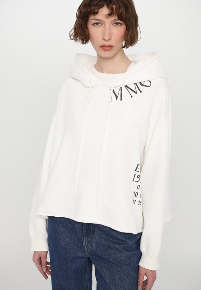 Λευκή κουκούλα φούτερ με μπροστινή τσέπη, κορδόνια και μαύρο εκτυπωμένο κείμενο μπροστά και στο μανίκι. Μαλακό, άνετο ύφασμα; cropped fit.