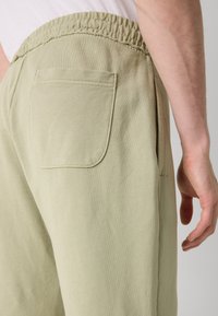 Helle grüne Hose mit elastischem Bund, ausgestattet mit einer Gesäßtasche und glatter Baumwollstruktur. Minimalistisches Design ohne sichtbare Muster.