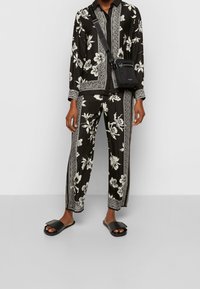 Zwart bloempatronen bijpassende blouse en broek met witte patronen, gemaakt van gladde stof. Gepaard met zwarte platte slip-on sandalen en een crossbody tas.