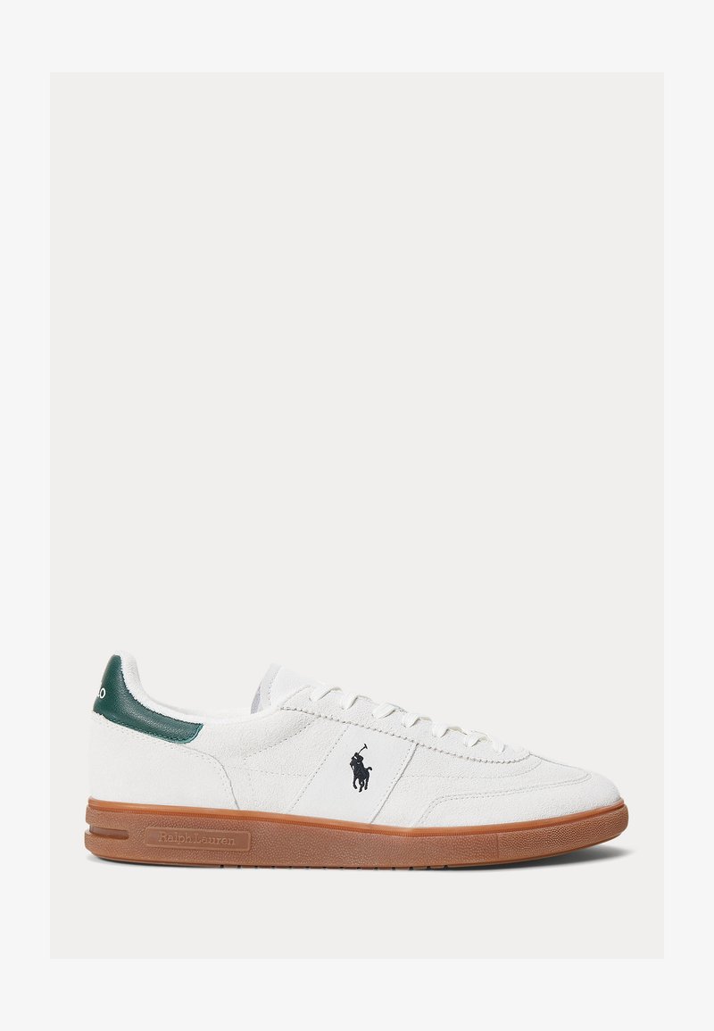 Witte suède lage sneaker met een bruine rubberen zool, groene hakaccent, zwart Polo Ralph Lauren-logo aan de zijkant en witte veters.