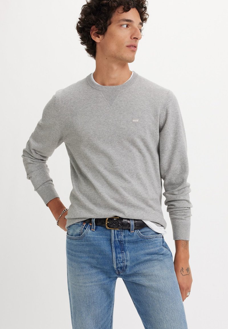 Gray long-sleeve sweatshirt with ribbed neckline, casual fit, worn with blue jeans and a braided black belt. Small logo on left chest.