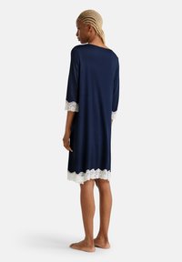 Camicetta da notte blu navy con maniche a tre quarti e bordi in pizzo bianco ai polsini e all'orlo. Realizzata in tessuto morbido e leggero.