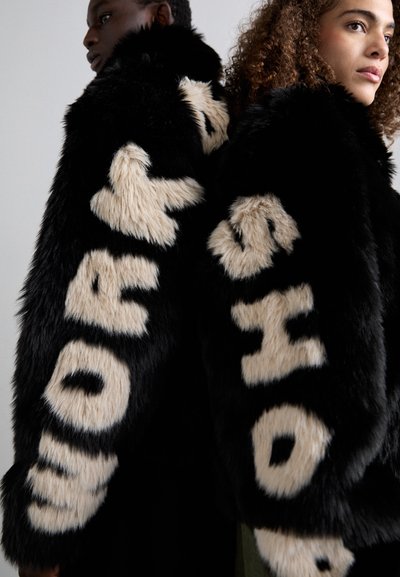 Chaqueta de pelaje sintético negro con atrevida letra beige, con una superficie suave y texturizada y corte holgado, vista en dos modelos.