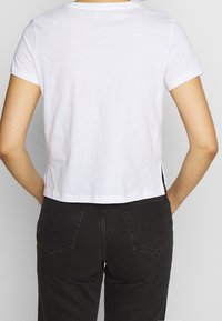 Hvid bomulds t-shirt med korte ærmer, let cropped design og rund halsudskæring. Bæres med højtsiddende sorte bukser.
