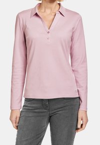 Langarm-Polohemd aus weichem pinken Stoff mit einem Notch-Kragen, drei Knöpfen und einer lockeren Passform. Kombiniert mit grauen Hosen.