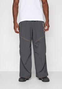 Pantaloni grigi da esterno con vestibilità ampia, caratterizzati da dettagli di cucitura gialla e tasche laterali. Realizzati in materiale leggero e traspirante.