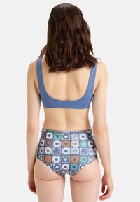 Bikini de talle alto con la parte de abajo estampada con gráficos florales en azul, naranja, verde y blanco, acompañado de un top azul sólido.