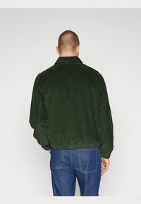 Groene corduroy jas met een kraag, met een gestructureerd oppervlak en een relaxte pasvorm, gecombineerd met blauwe denim jeans. Achteraanzicht getoond.