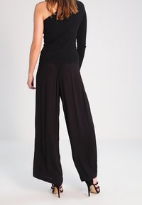 Top nero a coste con una spalla e manica lunga abbinato a pantaloni neri a gamba larga e sandali con tacco a strappo.