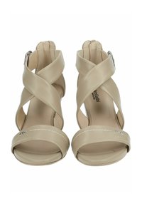 Sandali con tacco alto beige con cinturini incrociati realizzati in materiale sintetico liscio, caratterizzati da una punta arrotondata e dettagli cuciti.