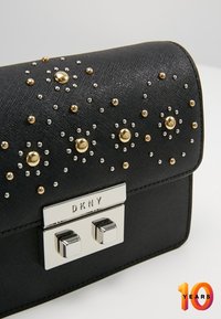 Black faux leather handbag featuring gold and silver studs in a floral design, with a polished silver clasp displaying "DKNY" branding.