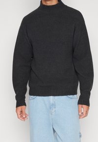 Maglione grigio scuro con collo alto, polsini e orlo a costine. Presenta una vestibilità comoda, realizzato in un materiale morbido e strutturato.