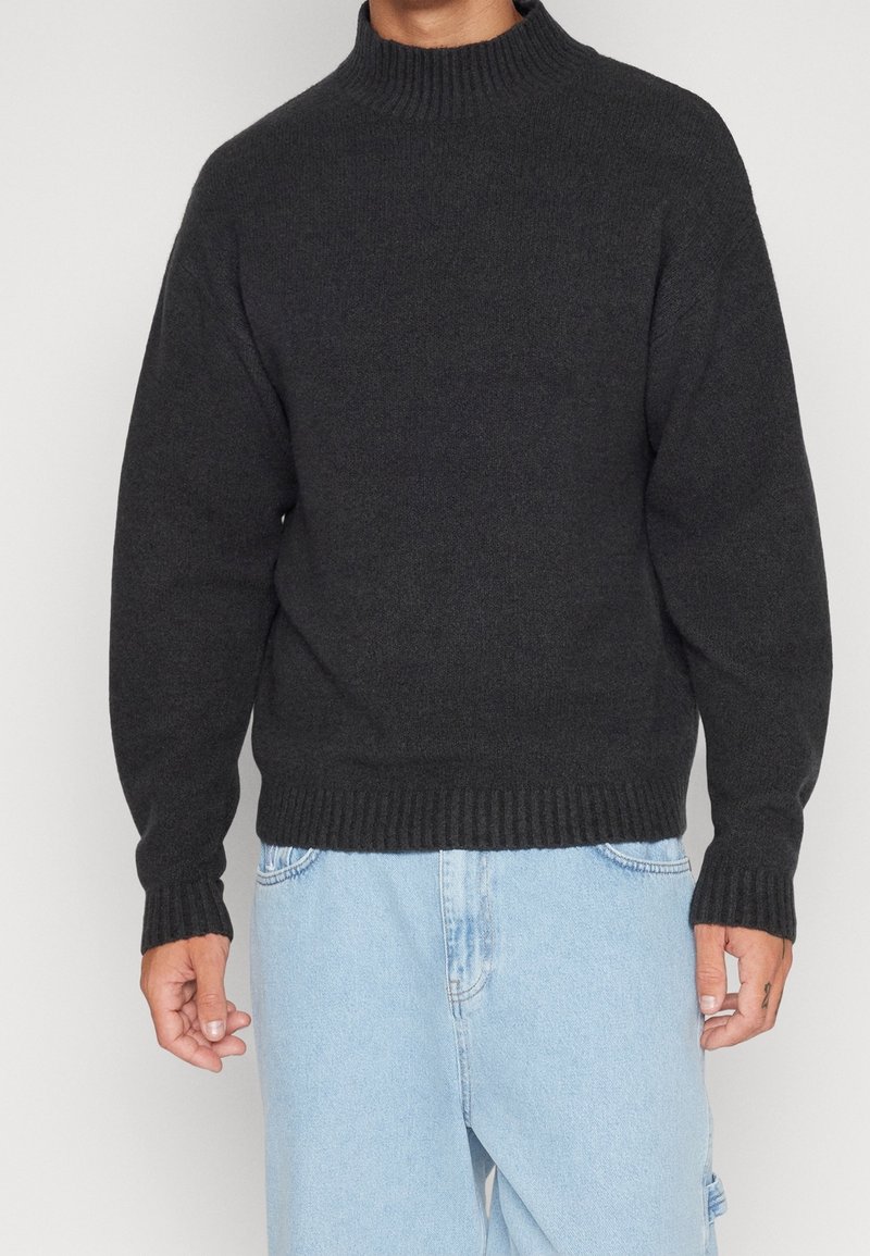 Maglione grigio scuro con collo alto, polsini e orlo a costine. Presenta una vestibilità comoda, realizzato in un materiale morbido e strutturato.