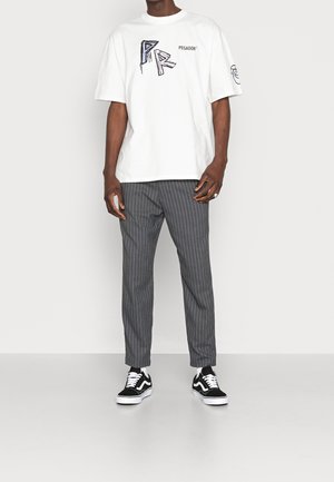 Weißes übergroßes T-Shirt mit schwarzem Grafiktext, kombiniert mit grauen Nadelstreifen-Hosen und schwarz-weißen Sneakers.