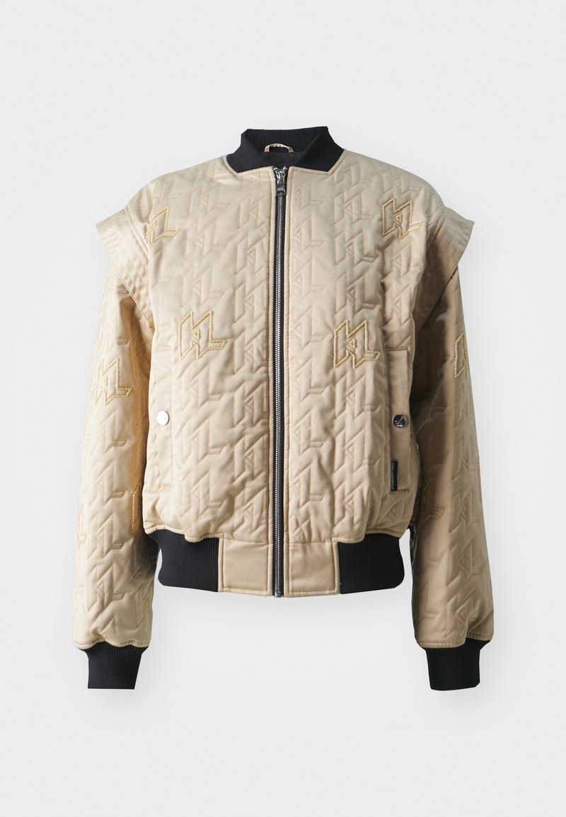 Beige gesteppte Bomberjacke mit Reißverschluss, schwarzen gerippten Bündchen und Kragen sowie goldenen, gestickten Logoakzenten auf dem Stoff.