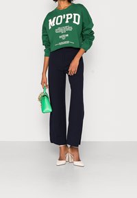 Zielona krótka bluza z białym nadrukiem, granatowe szerokie spodnie i beżowe szpilki. Trzymając małą zieloną torebkę z ozdobnym łańcuchem.