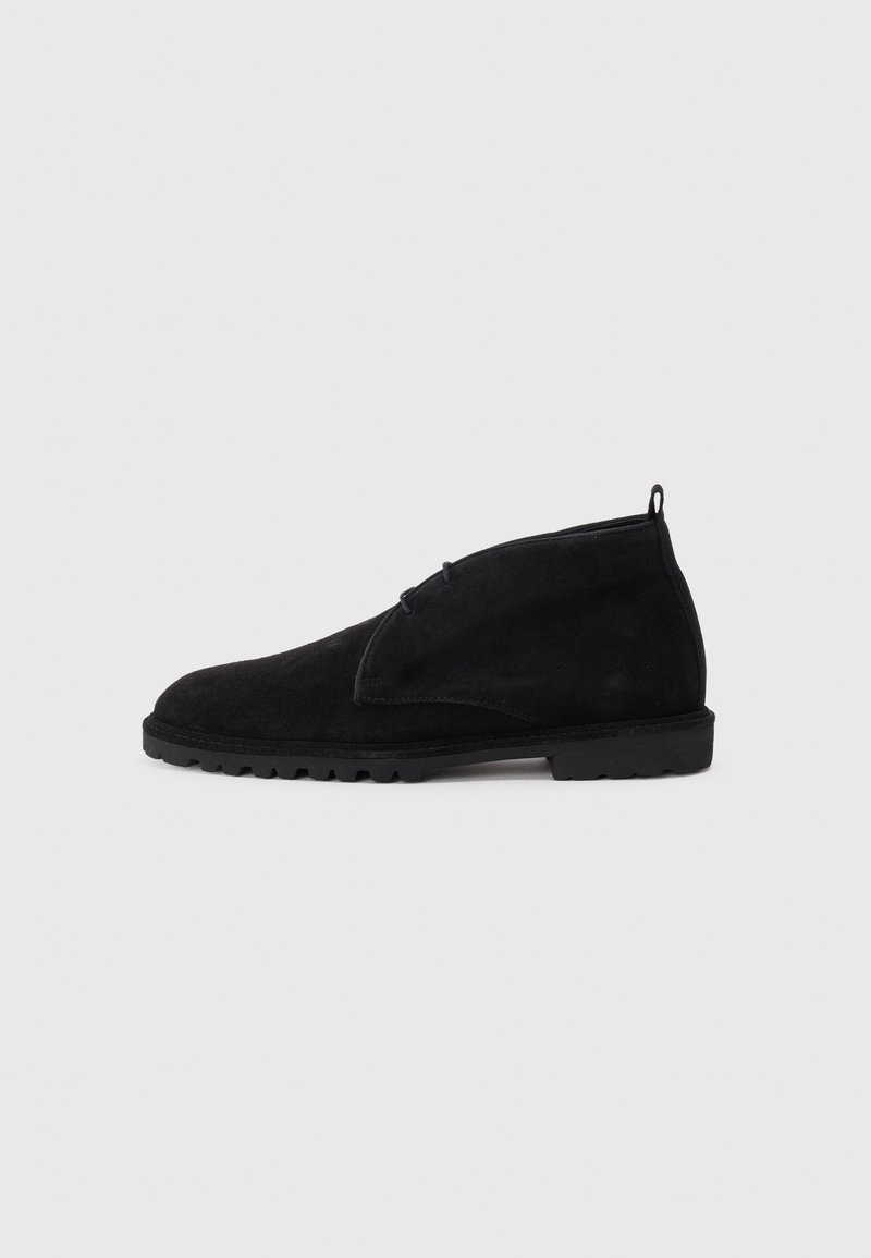 Stivali alla caviglia in suede nero con punta arrotondata, chiusura con lacci e suola in gomma texturizzata. Presentano un tassello sul retro.