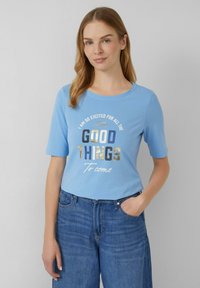 T-shirt bleu clair à manches courtes avec un slogan imprimé de différentes couleurs, de coupe décontractée et à col rond. Porté avec un pantalon en denim bleu.