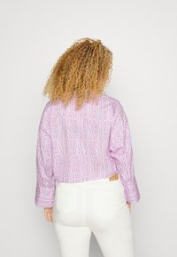 Camisa curta em lilás claro com um padrão geométrico; mangas longas, corte descontraído; combinada com jeans brancos com bolsos traseiros.