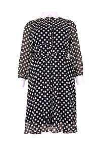 Schwarz-weiß gepunktetes Kleid mit weißen Punkten, durchsichtiger Stoff, lange Ärmel, Kragen mit Knopfverschluss, taillierter Schnitt und kontrastierende weiße Manschetten.