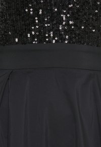 Robe noire avec un corsage à sequins et une ceinture unie au-dessus d'une jupe lisse et fluide.
