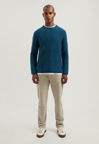 Blauwe gestructureerde gebreide trui met een ronde hals, gecombineerd met beige broeken en witte sneakers. Eenvoudig ontwerp met een ontspannen pasvorm.