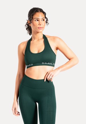 Reggiseno sportivo a coste verde scuro con ampia fascia brandizzata e collo all'americana. Abbinato a leggings coordinati a vita alta con testo laterale discreto.