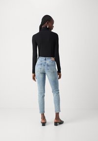 Maglietta nera a maniche lunghe abbinata a jeans slim-fit azzurri chiari. I jeans presentano un design con taschino posteriore e un'etichetta marrone in vita. Mule nere con tacco.