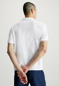 Polo shirt bianco a maniche corte realizzato in tessuto morbido e texture, con colletto piatto e vestibilità comoda, con orlo pulito.