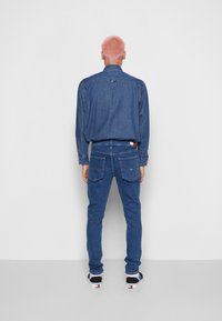 Camisa de mezclilla en azul oscuro con cuello abotonado y mangas largas, combinada con jeans de mezclilla azul a juego que cuentan con bolsillos traseros y costuras sutiles.