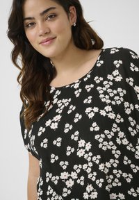 Blusa negra con estampado floral que presenta pequeñas flores blancas con acentos rojos, mangas cortas y un escote redondo. Tejido texturizado con un acabado suave.
