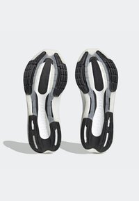 Zwart-witte zolen van sportschoenen met gestructureerde rubberen grip, een gladde witte tussenzool en "LIGHT BOOST" ingebosd aan de zijkant.