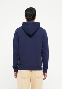 Navy blue hoodie with a drawstring hood, ribbed cuffs, and hem, made of soft fabric. Features a small logo tag at the bottom left.