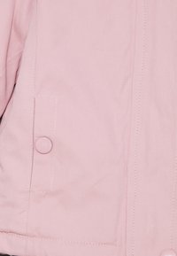 Světle růžová bunda vyrobená z hladkého materiálu, s knoflíkem a boční kapsou. Viditelné švy podél švů, jednoduchý design.