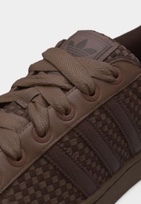 Baskets tissées marron Adidas avec des lacets épais, des œillets en cuir et le logo Adidas sur la languette.
