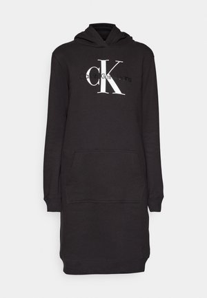 Mustan kapuutsiga pusakar dress, millel on ees tasku. Omab valget "Calvin Klein Jeans" logo ja pehmet, tekstuurset kangast. Pikad varrukad.