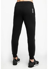 Pantaloni da jogging neri con taglio affusolato, cintura elastica, due tasche laterali e dettagli a strisce bianche sul retro. Realizzati in tessuto morbido.