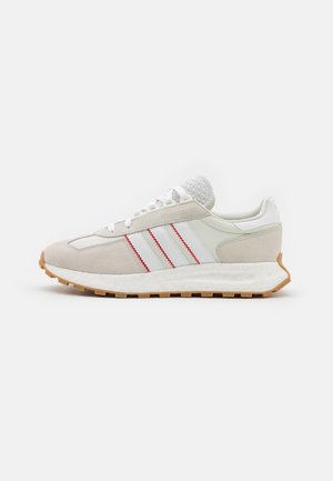 Biało-beżowy sneaker z gumową podeszwą, trzema białymi paskami z czerwonym przeszyciem oraz teksturowanym językiem na jednolitym białym tle.