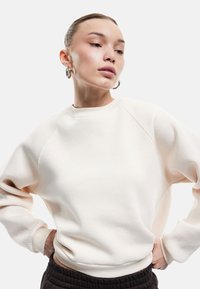 Jasno beżowy sweatshirt z okrągłym dekoltem, rękawami raglanowymi i ściągaczami. Wykonany z miękkiego materiału o gładkiej fakturze.