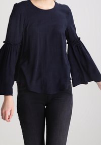 Blusa blu navy in tessuto leggero, con maniche a campana arricciate e scollatura rotonda con motivi di texture sottili.