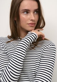 Fekete-fehér csíkos, hosszú ujjú felső, bordázott textúrával és magas nyakkal; az ujjak vége nyers szegéssel van ellátva.