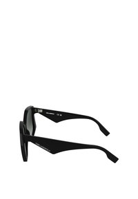 Zwarte zonnebril met een geometrische vorm, gekenmerkt door dikke monturen en schuine veren. De lenzen zijn donker en licht getint. "Karl Lagerfeld" logo aan de zijkant.