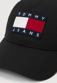 Svart baseballlue med et rektangulært Tommy Jeans-logo-patch som har hvite og røde fargeblokker på frontpanelet.
